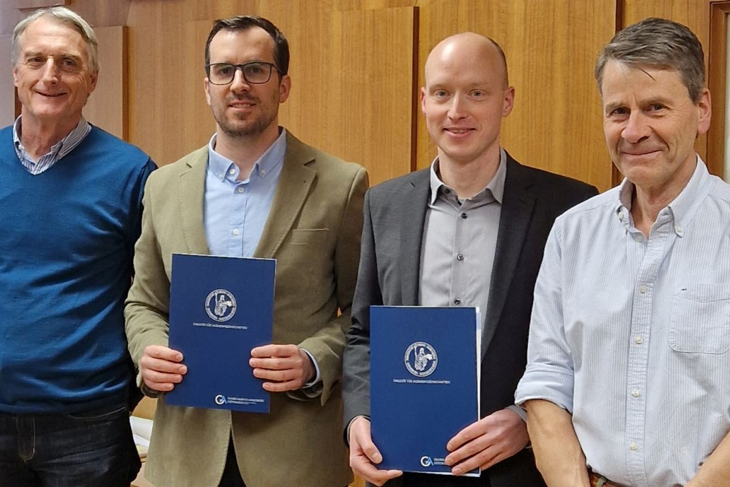 Vier Personen, 2 haben eine blaue Urkunde in der Hand