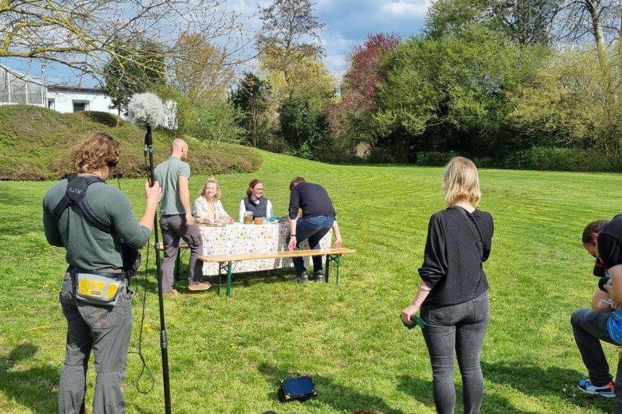 eine Gruppe an einem Tisch im Garten, im Vordergrund ein Filmteam